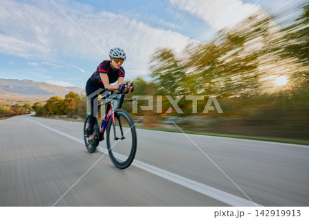 Female Road Cyclist Training at Speed on Open Country Road During Sunset Ride 142919913