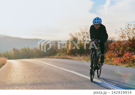 Female Cyclist Training on a Road Bike at Sunrise Through Scenic Autumn Countryside 142919914