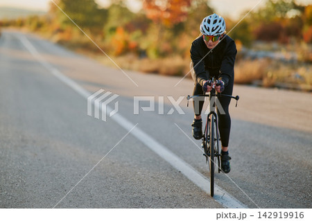 Female Cyclist Training on Open Road During Autumn Sunrise Workout 142919916