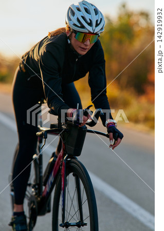 Female Cyclist Riding Road Bike At Sunset Training Outdoors With Helmet And Sunglasses 142919932