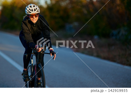 Female Road Cyclist Training At Sunset Wearing Helmet, Sunglasses And Cycling Gear Female Road Cyclist Training At Sunset Wearing Helmet, Sunglasses And Cycling Gear 142919935
