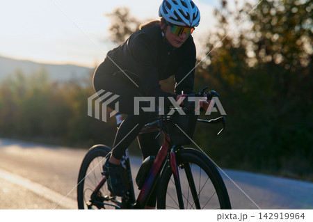 Female Cyclist Training on Road Bike at Sunset in Aerodynamic Racing Position 142919964
