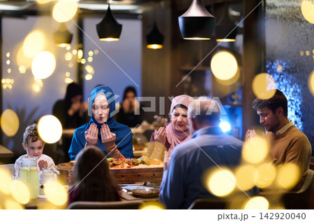 Muslim Family Praying Together at Dinner Table During Festive Evening Meal 142920040