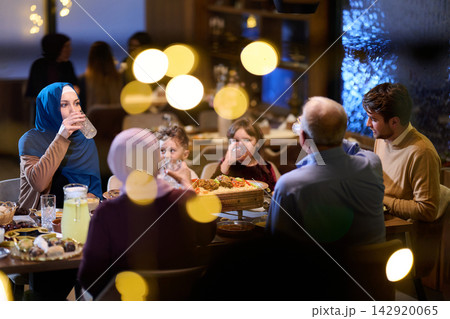 Family Dinner Gathering Around Table With Woman in Hijab, Children and Warm Restaurant Lighting 142920065