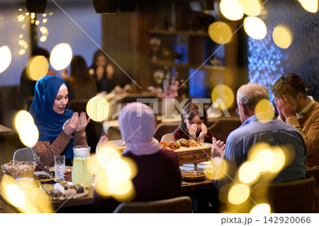 Muslim Family Praying Together Around Dinner Table During Ramadan Iftar Celebration 142920066