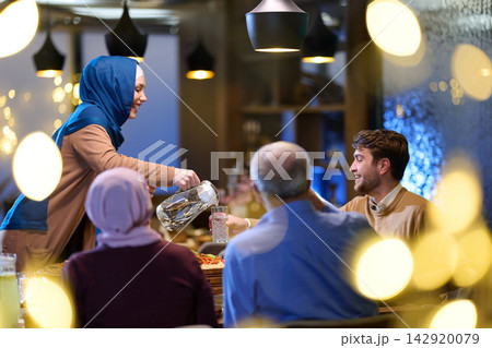Family Dinner With Woman in Headscarf Pouring Water at Festive Table 142920079