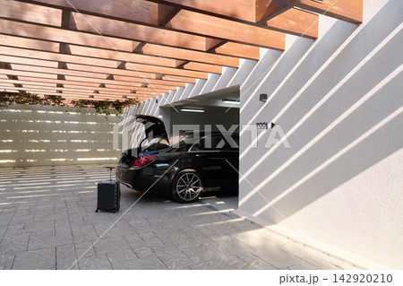 Luxury Sedan With Open Trunk and Luggage Parked in Modern Garage Near Pool at Sunny Resort Luxury Sedan With Open Trunk and Luggage Parked in Modern Garage Near Pool at Sunny Resort 142920210