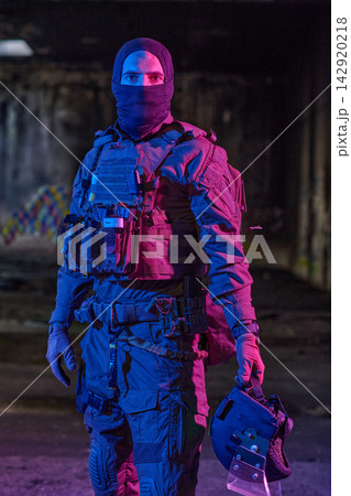Masked Tactical Soldier In Urban Gear Holding Helmet In Neon-Lit Abandoned Warehouse 142920218