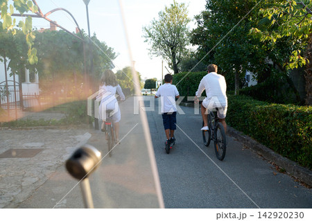 Family Biking and Scootering Together on a Quiet Residential Street During Summer Vacation Family Biking and Scootering Together on a Quiet Residential Street During Summer Vacation 142920230