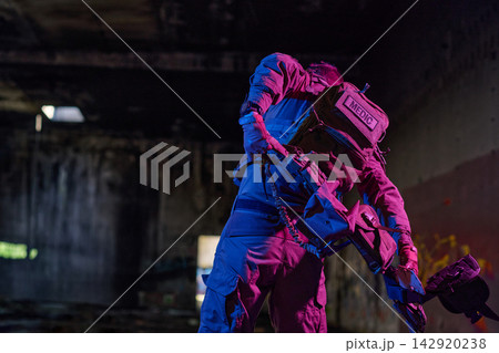 Tactical Medic In Gear Carrying Equipment Inside Dark Abandoned Urban Building With Neon Lighting Tactical Medic In Gear Carrying Equipment Inside Dark Abandoned Urban Building With Neon Lighting 142920238