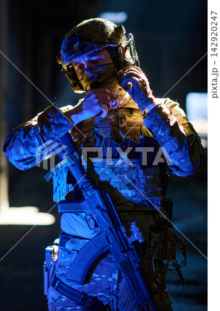 Soldier In Tactical Gear Adjusting Helmet And Radio During Night Operation With Assault Rifle 142920247