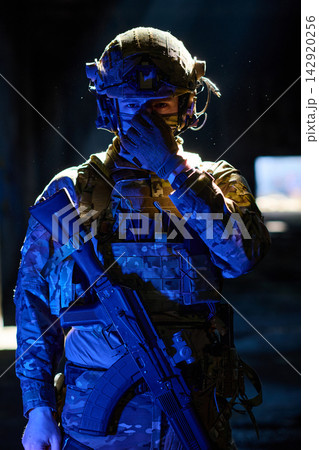 Armed Soldier in Tactical Gear and Helmet Holding Assault Rifle in Dramatic Low Light 142920256