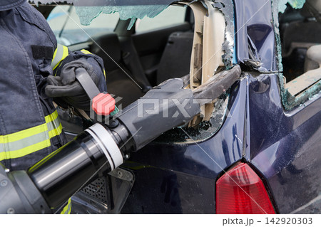 Firefighter Performing Vehicle Extrication With Hydraulic Cutter Using Jaws Of Life On Crashed Car Firefighter Performing Vehicle Extrication With Hydraulic Cutter Using Jaws Of Life On Crashed Car 142920303