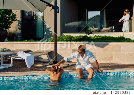 Father And Son At A Luxury Villa Pool With Woman On Balcony During Sunny Summer Morning Father And Son At A Luxury Villa Pool With Woman On Balcony During Sunny Summer Morning 142920382