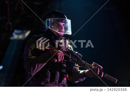 Armed Tactical Operator in Riot Helmet and Ballistic Visor Holding Rifle in Low-Light Environment 142920388