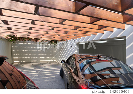 Modern Car Parked Under Wooden Pergola Garage With Dramatic Light And Shadow Patterns 142920405