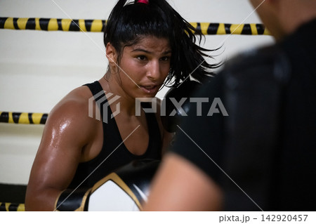 Determined Female Boxer Training in Ring During Intense Sparring Session With Coach 142920457