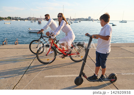 Family Cycling By The Seafront With Boy On Electric Scooter During Sunny Summer Vacation Family Cycling By The Seafront With Boy On Electric Scooter During Sunny Summer Vacation 142920938