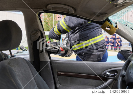 Firefighter Performing Vehicle Extrication With Hydraulic Cutter During Emergency Rescue Training Drill Firefighter Performing Vehicle Extrication With Hydraulic Cutter During Emergency Rescue Training Drill 142920965