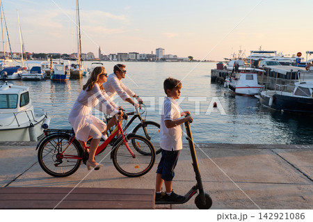 Family Cycling and Electric Scooter By The Harbor At Sunset During Summer Vacation 142921086