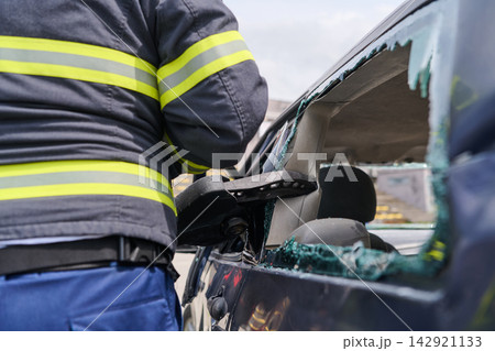 Firefighter Performing Car Rescue at Crash Scene With Broken Glass and Damaged Vehicle Firefighter Performing Car Rescue at Crash Scene With Broken Glass and Damaged Vehicle 142921133