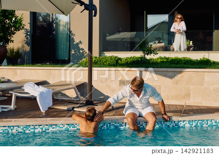 Family Morning By The Pool: Father With Son At Luxury Villa While Mother Watches From Balcony Family Morning By The Pool: Father With Son At Luxury Villa While Mother Watches From Balcony 142921183