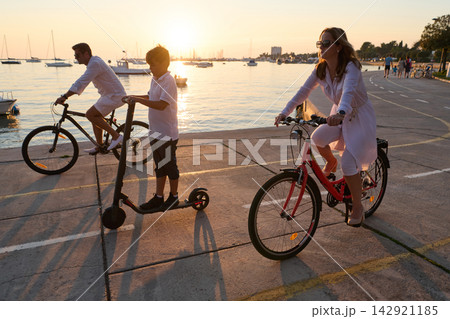 Family Cycling and Scooting Along Seafront Promenade at Sunset Near Boats and Harbor Family Cycling and Scooting Along Seafront Promenade at Sunset Near Boats and Harbor 142921185