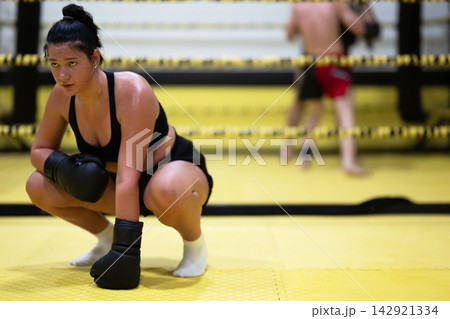 Female Boxer Resting in Ring After Intense Training Session in Yellow Gym With Boxing Gloves 142921334