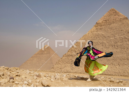 Whirling performer caught mid spin with a dramatic billowing multicolor patchwork cape against the iconic Giza Pyramids on the desert plateau in bold Whirling performer caught mid spin with a dramatic billowing multicolor patchwork cape against the iconic Giza Pyramids on the desert plateau in bold 142921364