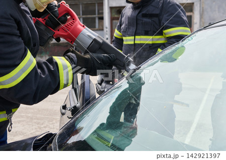 Firefighters Performing Vehicle Extrication Using Power Saw To Remove Cracked Windshield After Car Accident Firefighters Performing Vehicle Extrication Using Power Saw To Remove Cracked Windshield After Car Accident 142921397