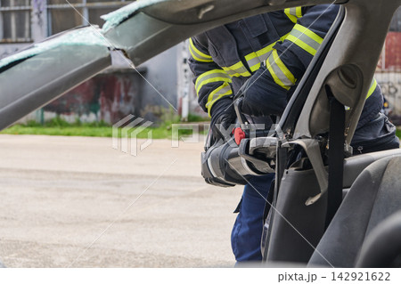 Firefighter Using Hydraulic Rescue Tool To Extricate Passenger From Crashed Car During Emergency Response 142921622