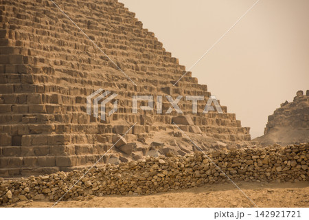 Close low angle view of pyramid limestone blocks and ancient rubble retaining wall at Giza plateau under dusty overcast sky ideal for archaeology Close low angle view of pyramid limestone blocks and ancient rubble retaining wall at Giza plateau under dusty overcast sky ideal for archaeology 142921721