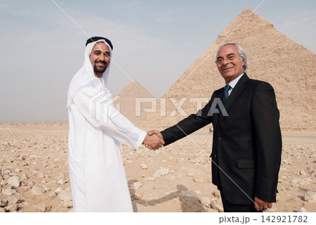 Cross cultural business handshake between Arab executive in thobe and senior Western professional before Giza Pyramids Egypt desert Cross cultural business handshake between Arab executive in thobe and senior Western professional before Giza Pyramids Egypt desert 142921782