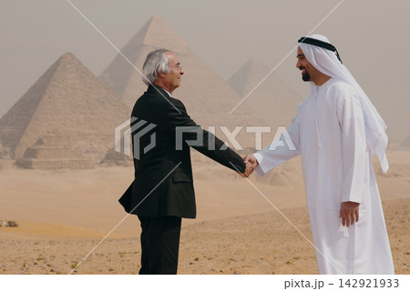 Cross cultural business handshake between Arab professional in kandura and senior Western executive at Giza pyramids Egypt ideal for international Cross cultural business handshake between Arab professional in kandura and senior Western executive at Giza pyramids Egypt ideal for international 142921933