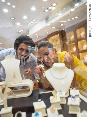 Happy couple shopping for jewelry together at an upscale jewelry store display case Happy couple shopping for jewelry together at an upscale jewelry store display case 142922030