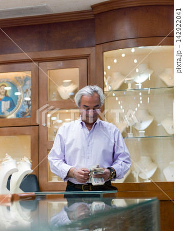 Jewelry shop owner counting cash behind the glass display in a luxury boutique Jewelry shop owner counting cash behind the glass display in a luxury boutique 142922041