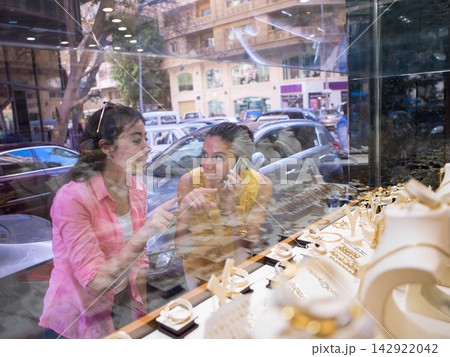 Two friends window shopping for jewelry and discussing a display while one talks on the phone Two friends window shopping for jewelry and discussing a display while one talks on the phone 142922042