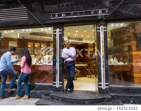 Jeweller standing at storefront of elegant jewellery shop while customers browse display windows on street Jeweller standing at storefront of elegant jewellery shop while customers browse display windows on street 142922092