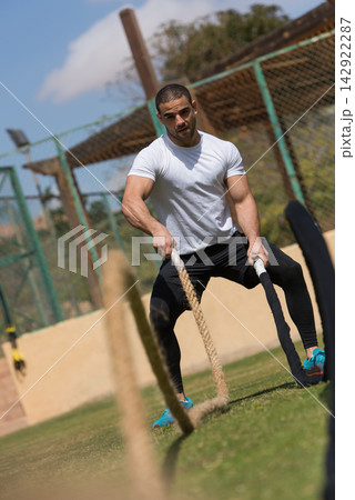 Athletic man doing outdoor battle ropes workout at a fitness training facility on a sunny day Athletic man doing outdoor battle ropes workout at a fitness training facility on a sunny day 142922287