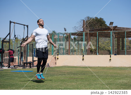 Middle Eastern man jumping rope during outdoor CrossFit workout at open-air fitness gym with friend Middle Eastern man jumping rope during outdoor CrossFit workout at open-air fitness gym with friend 142922385