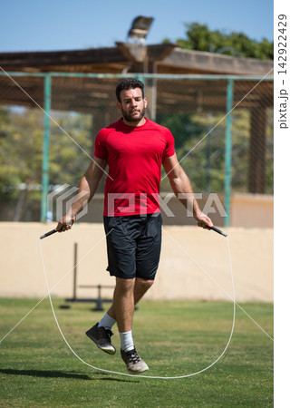 Man jumping rope during outdoor fitness training session at an open air gym for cardio and strength Man jumping rope during outdoor fitness training session at an open air gym for cardio and strength 142922429