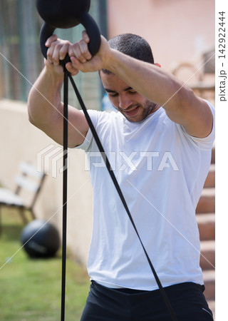 Middle Eastern Arab man doing outdoor CrossFit workout with resistance band and kettlebell Middle Eastern Arab man doing outdoor CrossFit workout with resistance band and kettlebell 142922444