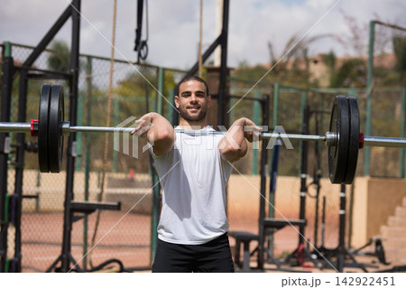 Man lifting barbell at outdoor CrossFit gym during strength training with a workout partner Man lifting barbell at outdoor CrossFit gym during strength training with a workout partner 142922451