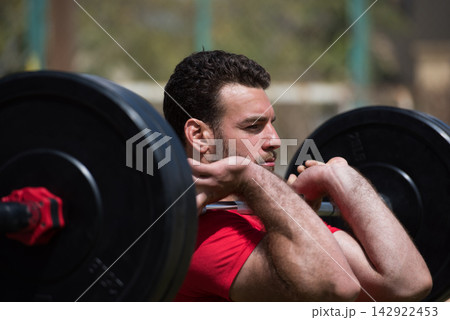 Arab man performing front squat with barbell in an outdoor CrossFit gym with a friend Arab man performing front squat with barbell in an outdoor CrossFit gym with a friend 142922453