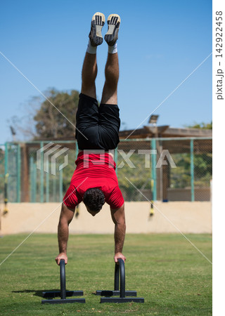 Middle Eastern man performing handstand push-up on parallettes in outdoor CrossFit gym workout Middle Eastern man performing handstand push-up on parallettes in outdoor CrossFit gym workout 142922458