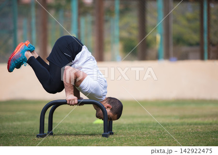 Outdoor fitness workout: man performing advanced CrossFit bodyweight exercise on parallette bars Outdoor fitness workout: man performing advanced CrossFit bodyweight exercise on parallette bars 142922475