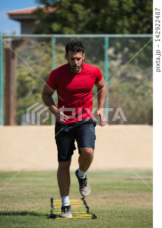 Man doing outdoor agility ladder workout for fitness and speed training on grass field 142922487