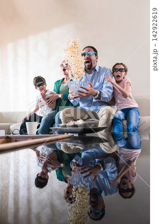 Family on couch surprised as popcorn explodes while watching movie together in cozy living room 142922619