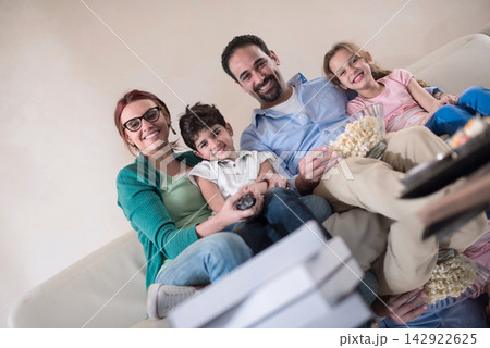 Modern Middle Eastern Arab family enjoying movie night together on the sofa with popcorn and remotes Modern Middle Eastern Arab family enjoying movie night together on the sofa with popcorn and remotes 142922625