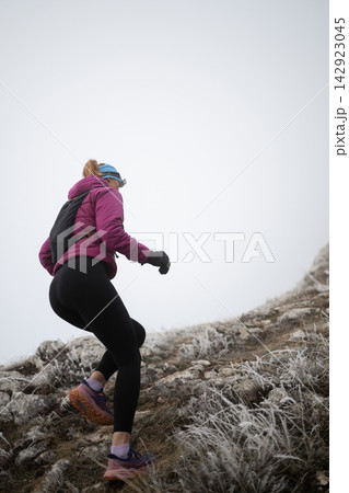 Woman Hiking Uphill on Frosty Mountain Trail in Winter Gear for Outdoor Fitness Adventure Woman Hiking Uphill on Frosty Mountain Trail in Winter Gear for Outdoor Fitness Adventure 142923045